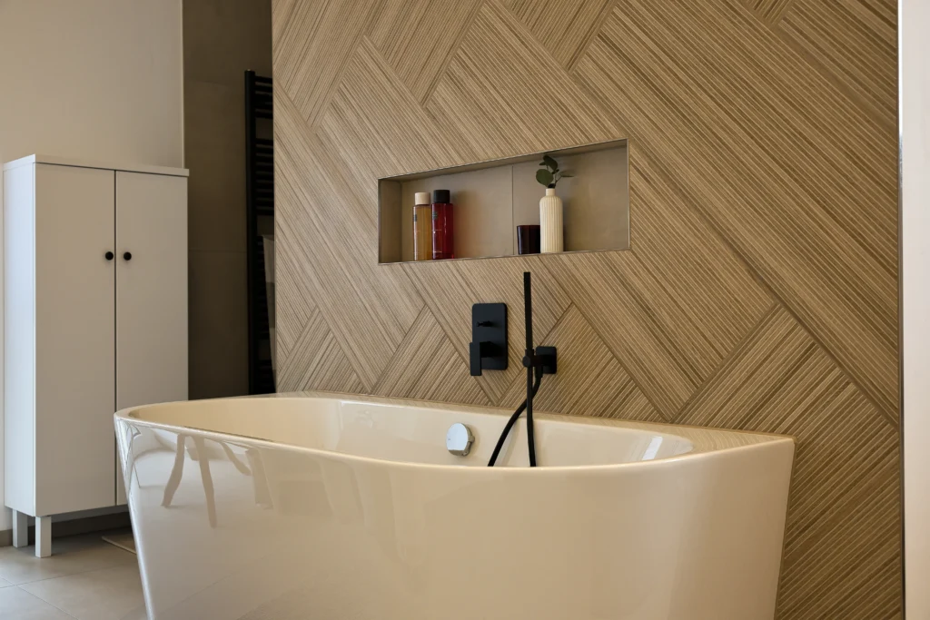 Freistehende Badewanne mit schwarzer Armatur, Wandnische und Holzoptikfliesen – Vatter Badstudio