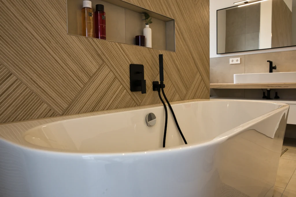 Detailansicht einer freistehenden Badewanne mit schwarzer Armatur und strukturierter Holzoptikfliese – Vatter Badstudio