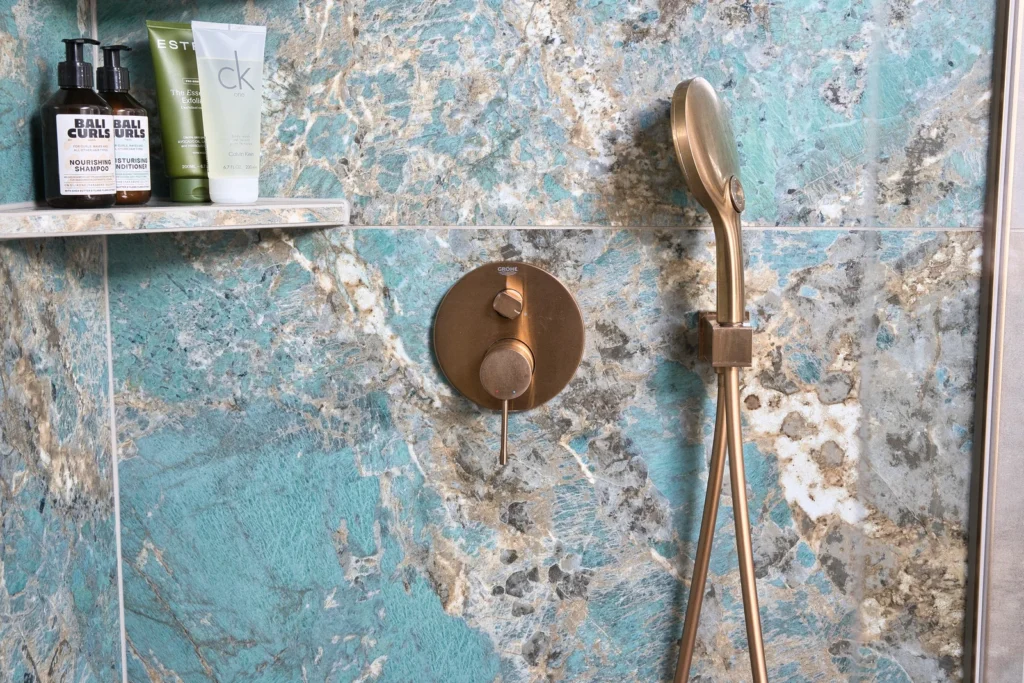 Grohe Duscharmatur in Gold vor Wandfliese in Natursteinoptik