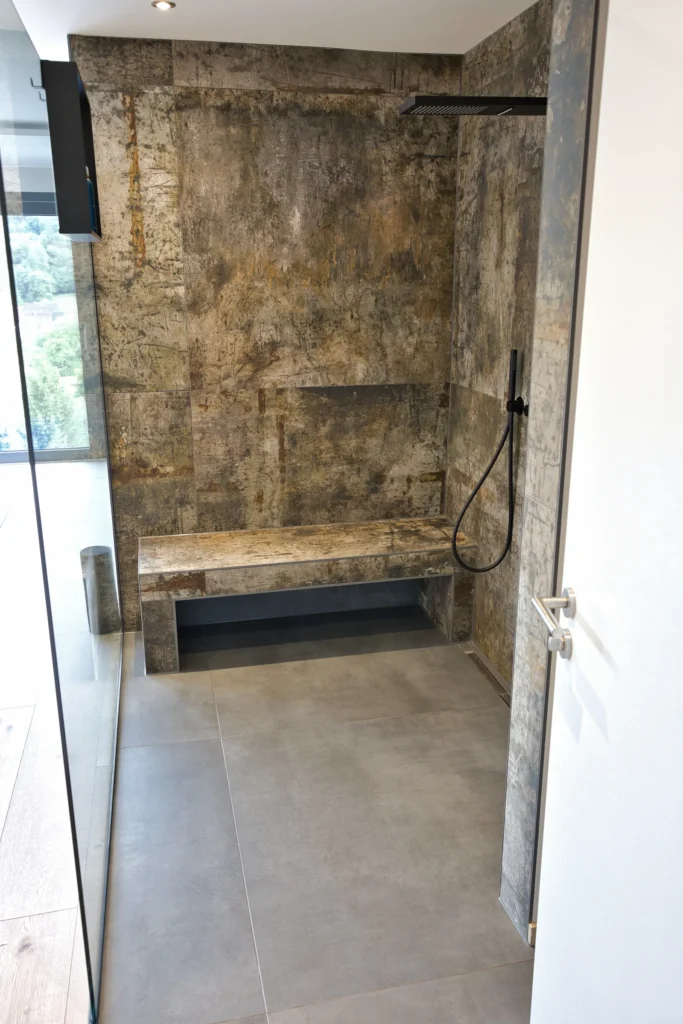 Großzügige Dusche mit Sitzbank, Natursteinoptik-Fliesen und schwarzen Armaturen – Vatter Badprojekt