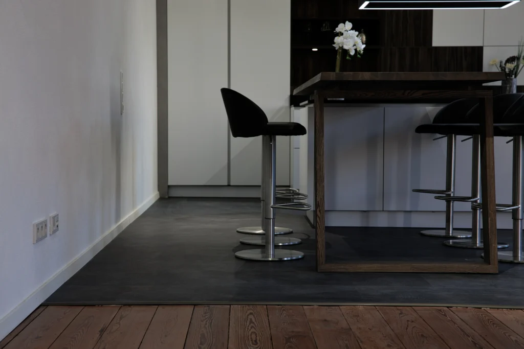 Übergang von Holzboden zu dunklem Vinylboden mit moderner Küchentheke und Barhockern
