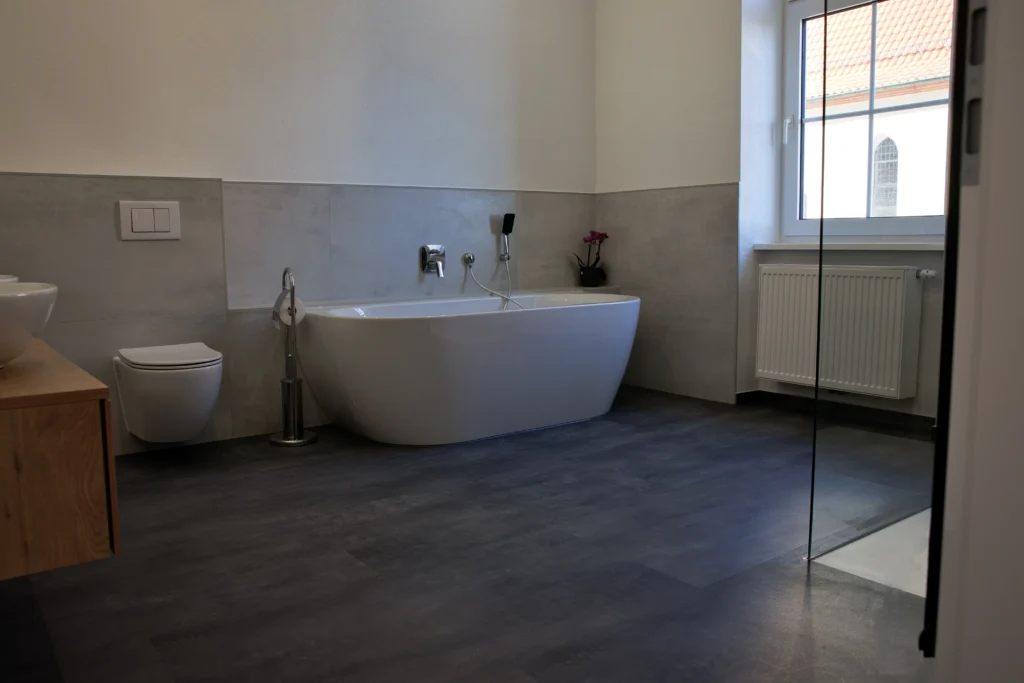 Modernes Bad mit freistehender Badewanne, Wandfliesen in Betonoptik und dunklem Boden
