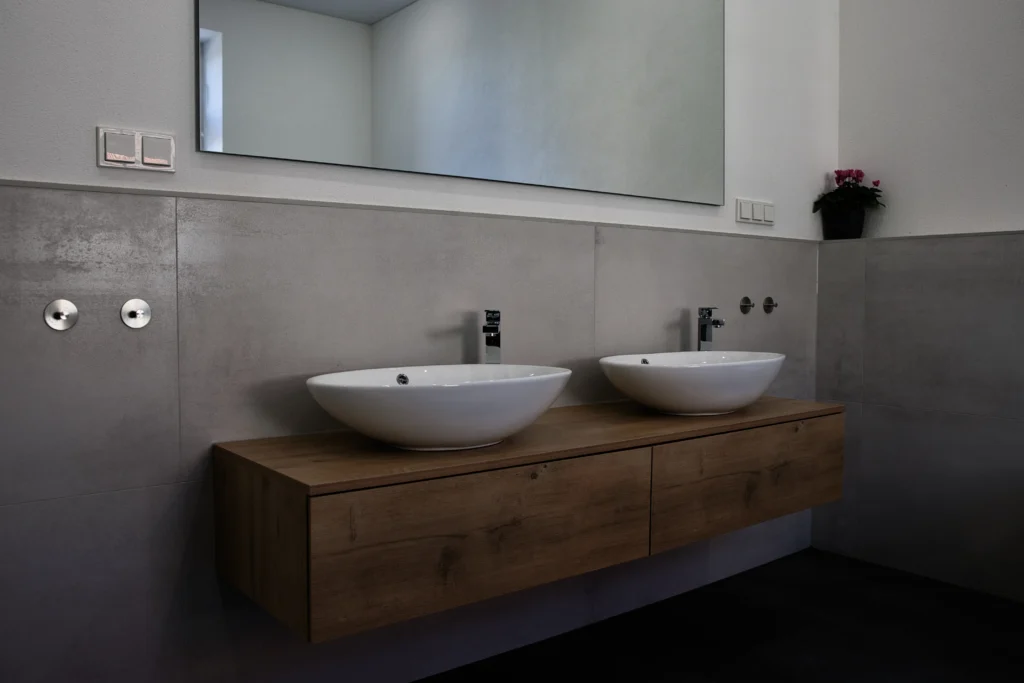 Modernes Badezimmer mit Doppelwaschtisch aus Holz und Aufsatzwaschbecken vor Wandfliesen in Betonoptik
