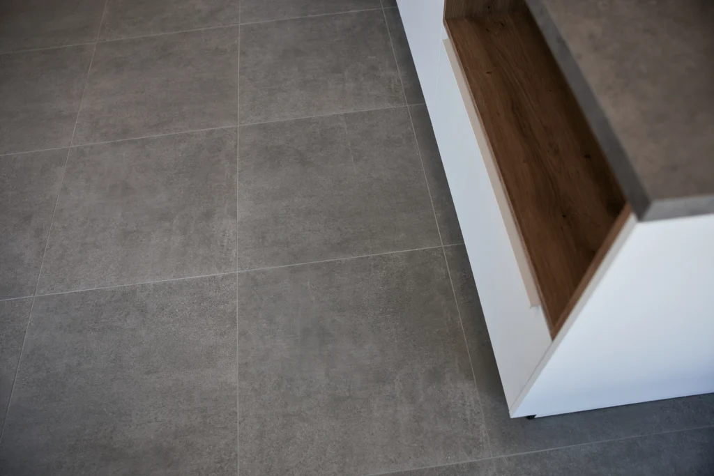 Detailaufnahme grauer Bodenfliesen neben heller Küchenzeile