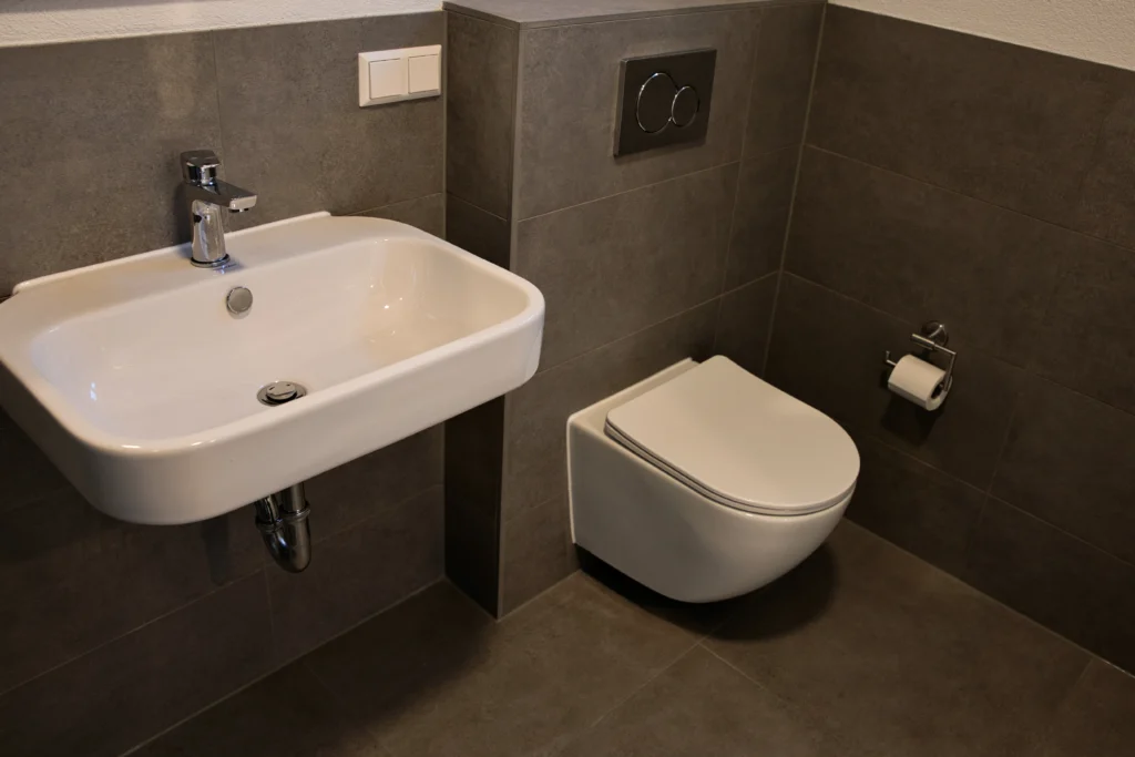 Bad mit grauen Fliesen, wandhängendem WC und schlichtem Waschbecken