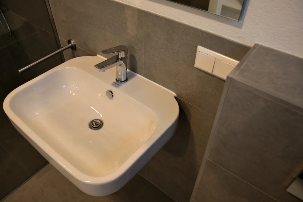Waschbecken mit moderner Armatur vor grauer Wandfliese im Bad