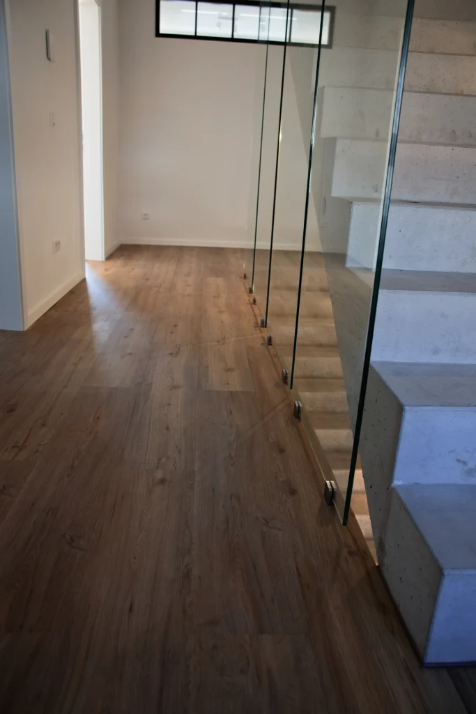 Moderner Flur mit Holzoptikboden und Betontreppe mit Glasgeländer