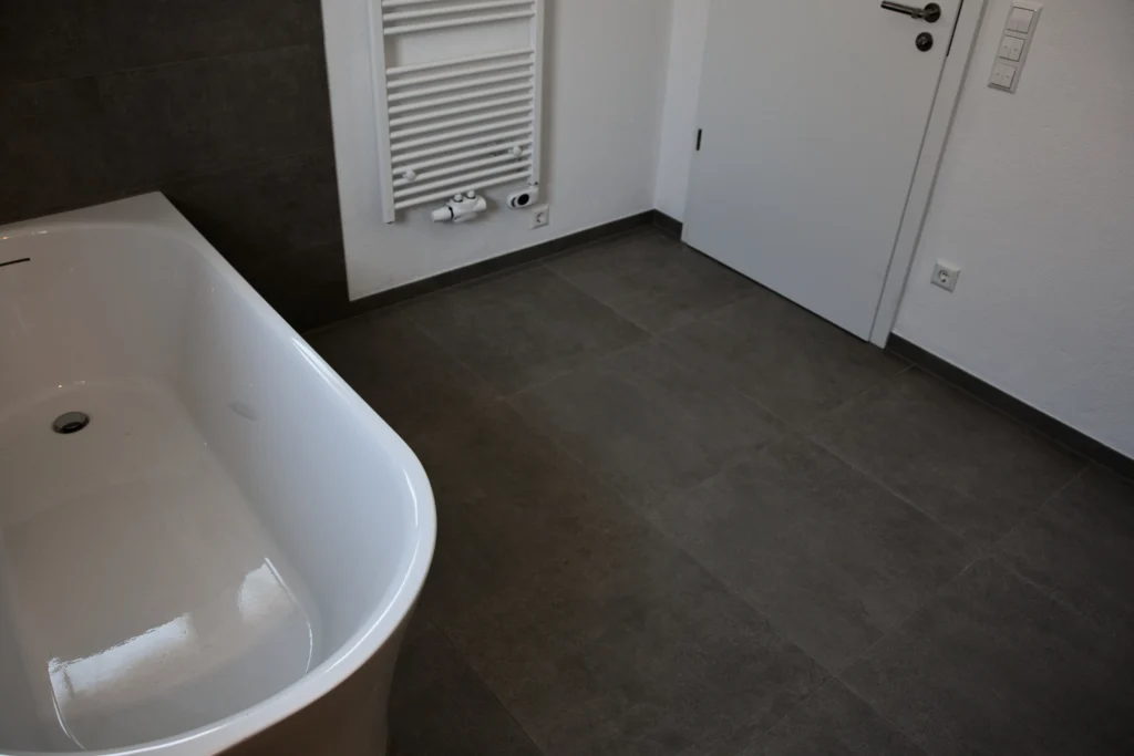 Bad mit freistehender Wanne, grauen Bodenfliesen und weißer Tür