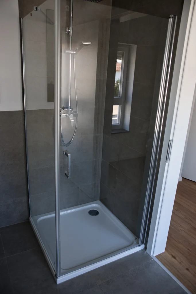 Eckdusche mit Glasabtrennung und grauen Wandfliesen im modernen Bad