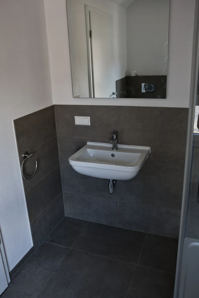 Kleines Badezimmer mit Wand- und Bodenfliesen in Grautönen und modernem Waschbecken