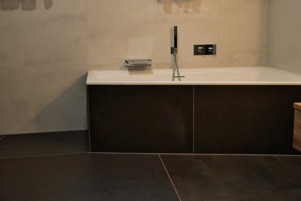 Badewanne mit dunkler Metalloptik Bodenfliese kombiniert mit heller Betonoptik Wandfliese