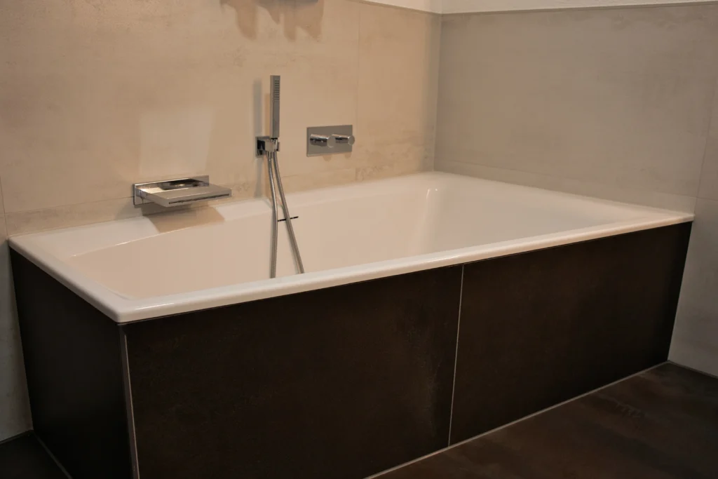 Detailansicht Badewanne mit Metalloptik Bodenfliese und heller Betonoptik im Wandbereich