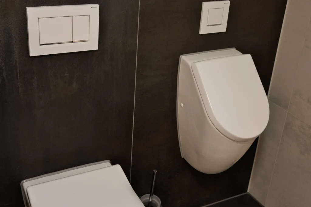 Detailaufnahme von WC und Bidet vor dunkler Feinsteinzeugfliese in Metalloptik