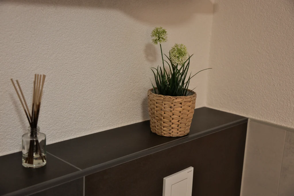 Vorwandinstallation im Bad mit dunkler Metalloptik-Fliese und integrierter Ablagefläche