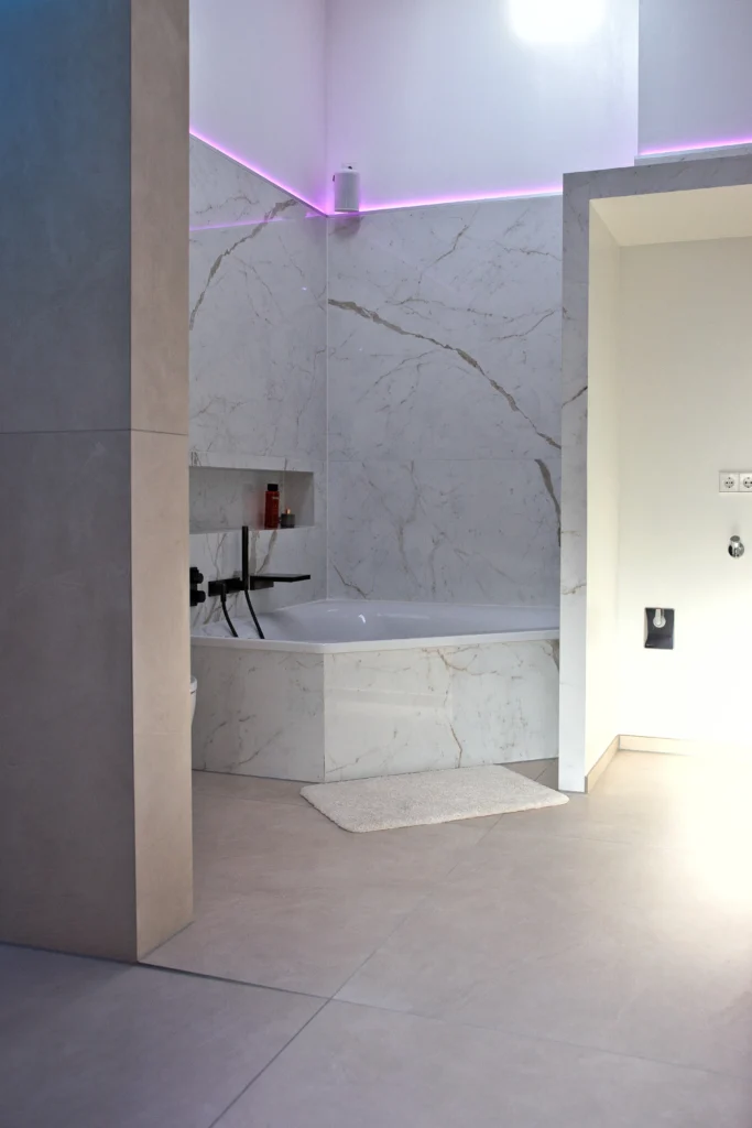 Luxuriöse Badewanne im Spa-Bad mit marmorierter Natursteinoptik Calacatta, indirekter LED-Lichtlinie und ruhiger Farbgestaltung