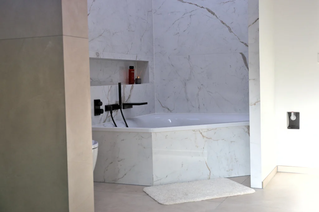 Badewanne mit Wandnische, Herzbach Armatur in Dark Platinum matt und marmorierter Fliese in Calacatta Natursteinoptik