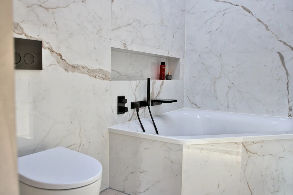 Detailaufnahme Badewanne mit Herzbach Wannenarmatur Dark Platinum matt und großformatiger Fliese Calacatta Prestigio