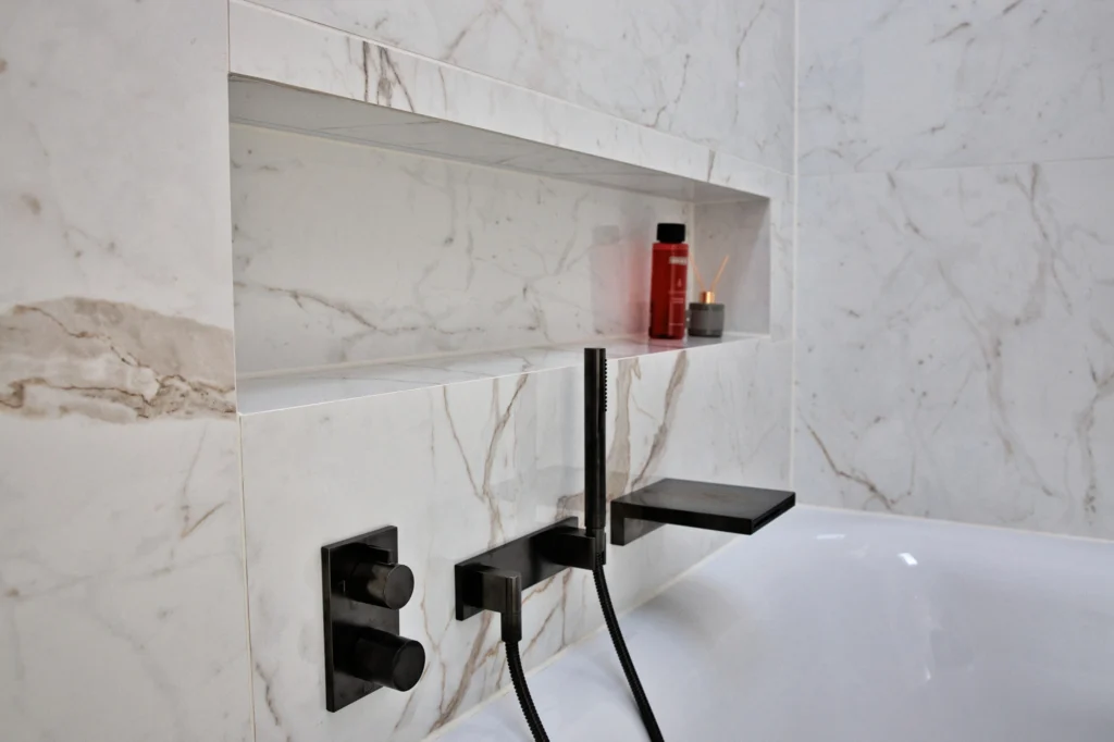 Praktische Wandnische über der Badewanne in Marmoroptik mit schwarzen Designarmature