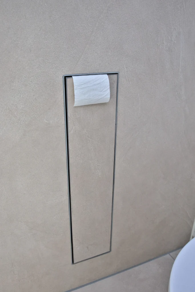 Bündig integrierter Toilettenpapierhalter vor großformatiger Boden- und Wandfliese in Natursteinoptik Prism Cord