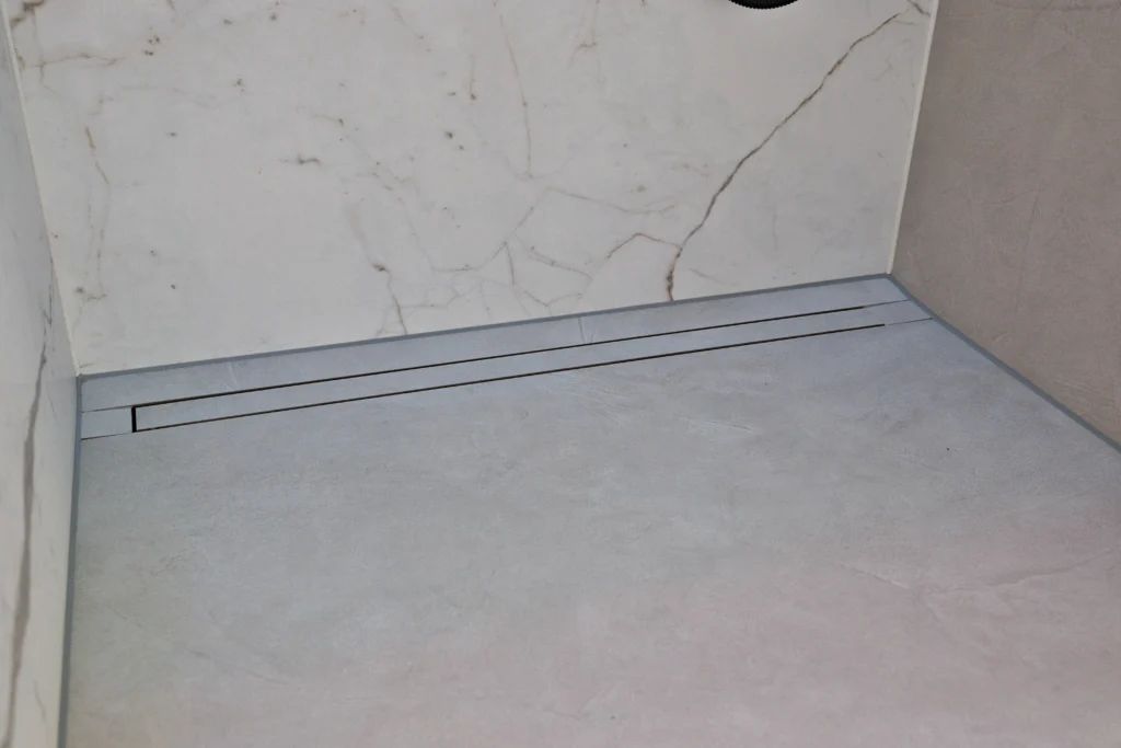 Bodenebene Linienentwässerung in der Dusche mit großformatigen Fliesen in Marmoroptik an der Wand und Betonoptik am Boden